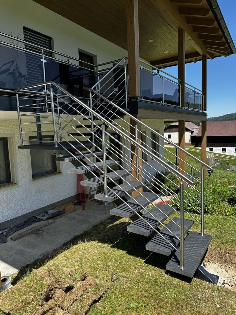Eine Mittelholmtreppe mit Metall Geländer führt von einem Balkon zu einem Garten