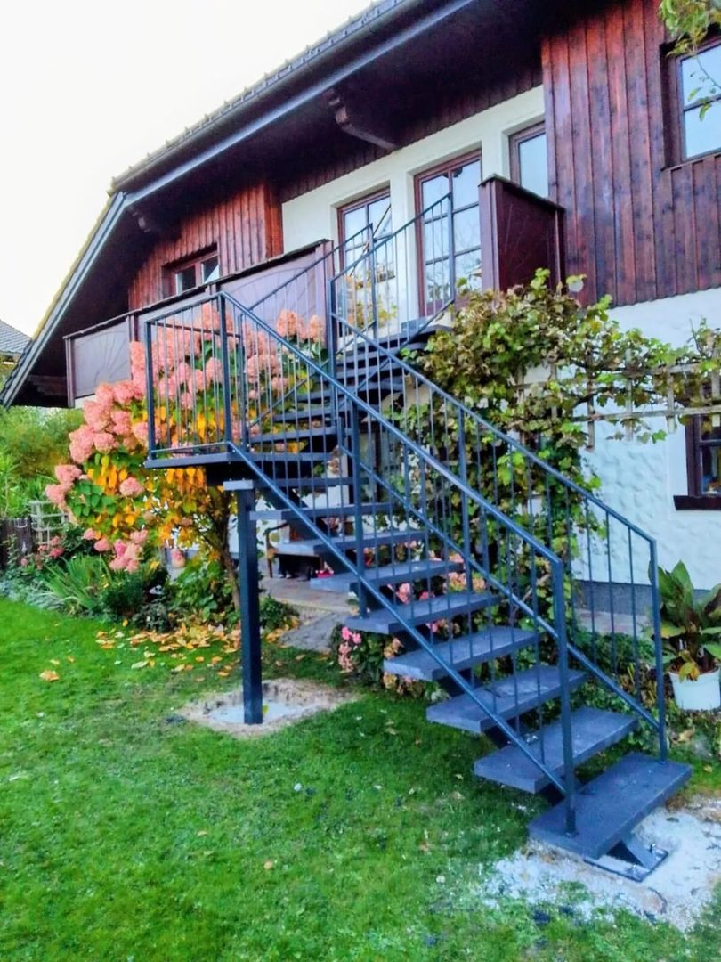 Eine schwarze Mittelholmtreppe mit Metall Geländer führt zu einem Garten