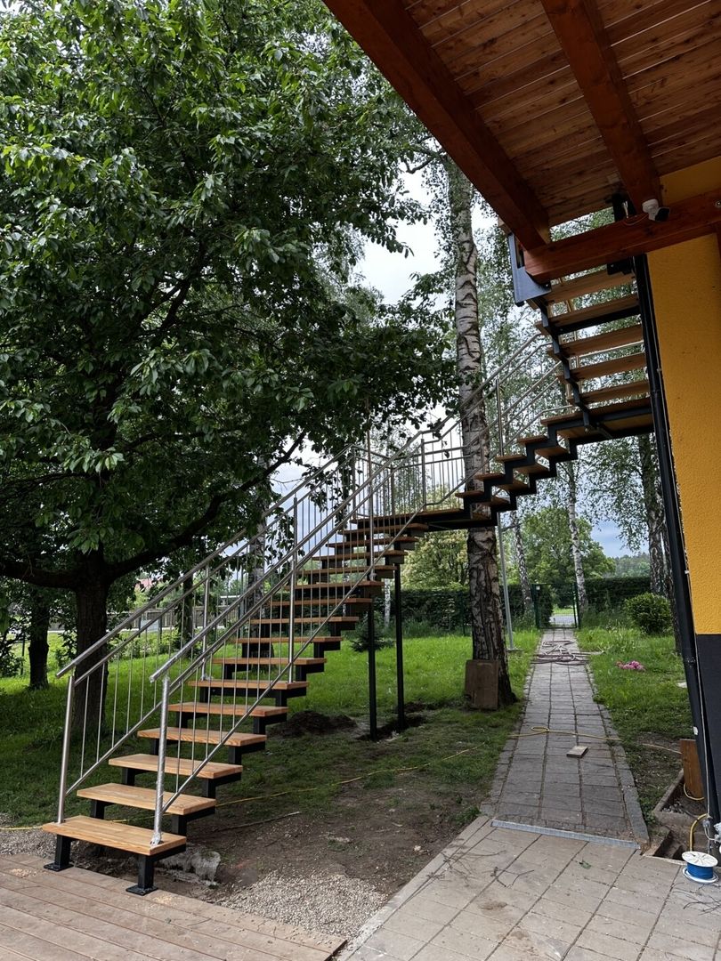Eine freistehende Zweiholmtreppe aus Holz mit zwei Zwischenpodesten führt zu einem Holzhaus