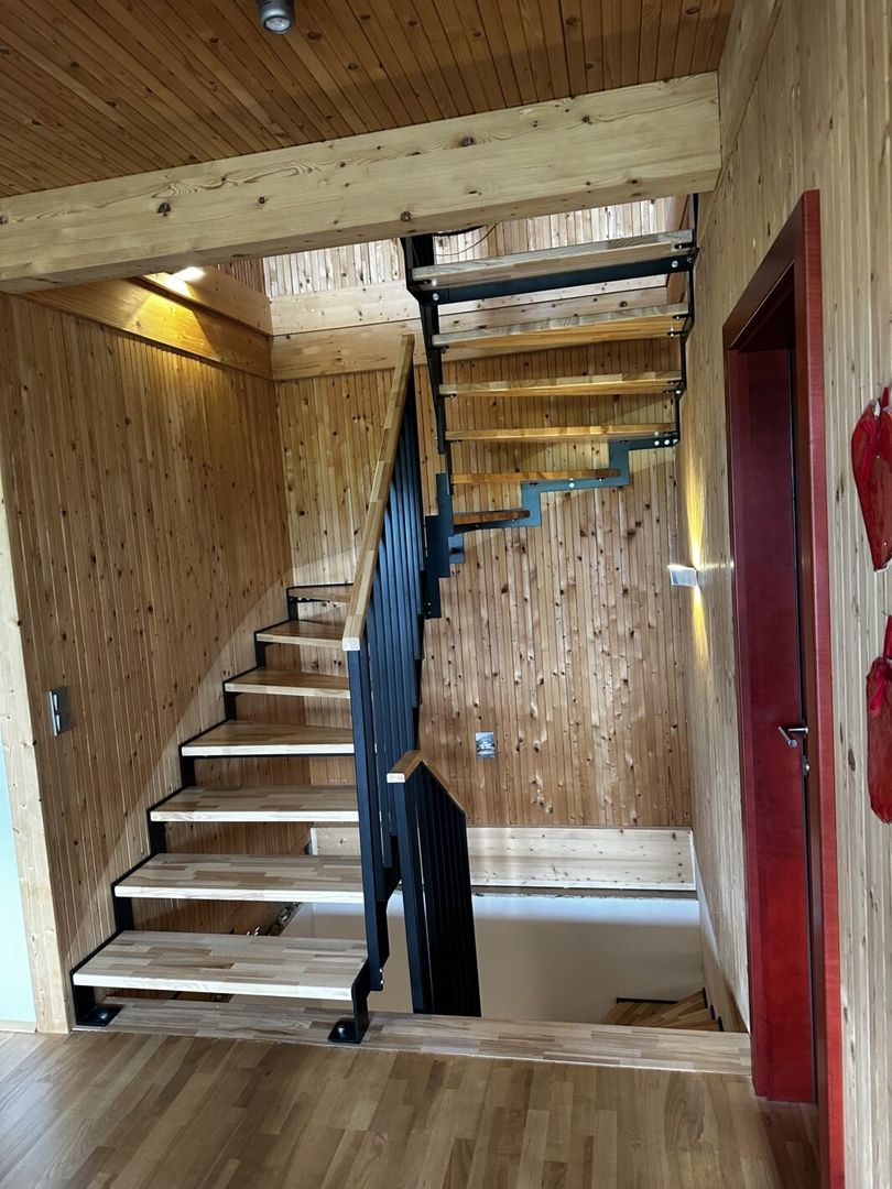 Eine Stahlwangentreppe mit einem Stabgeländer und Holztreppen in einem Flur mit Holzboden und Holzwänden