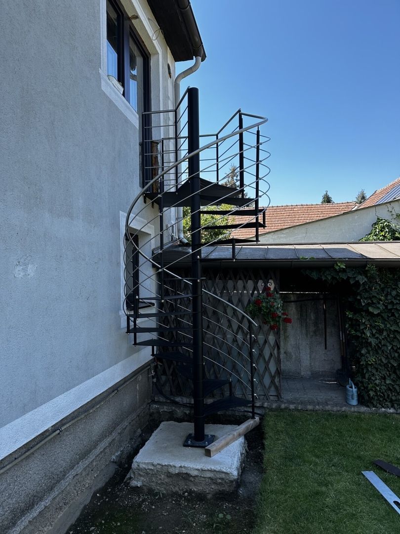 Eine schwarze Edelstahl Spindeltreppe die vom Garten in eine Tür am Haus führt