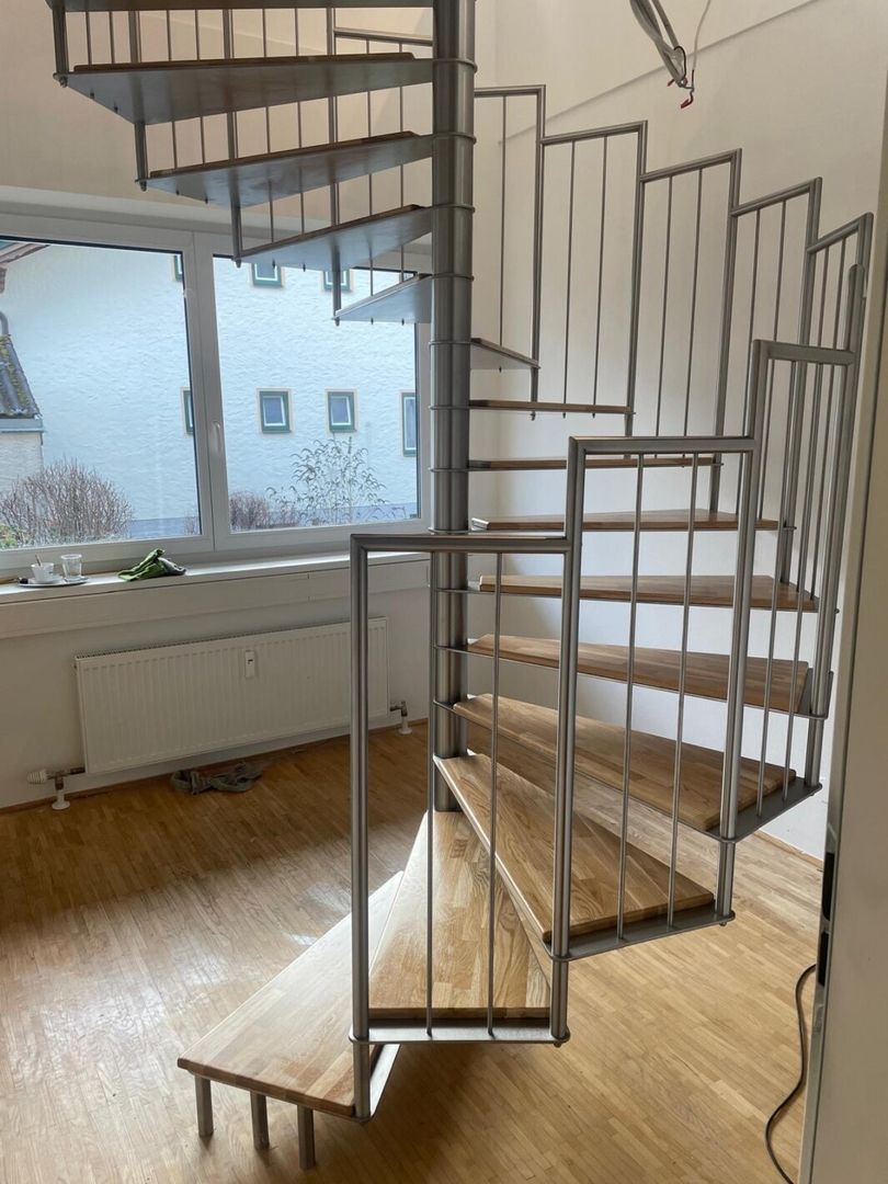Eine Spindeltreppe aus Holz mit Metallgeländer steht in einem hellen Wohnzimmer