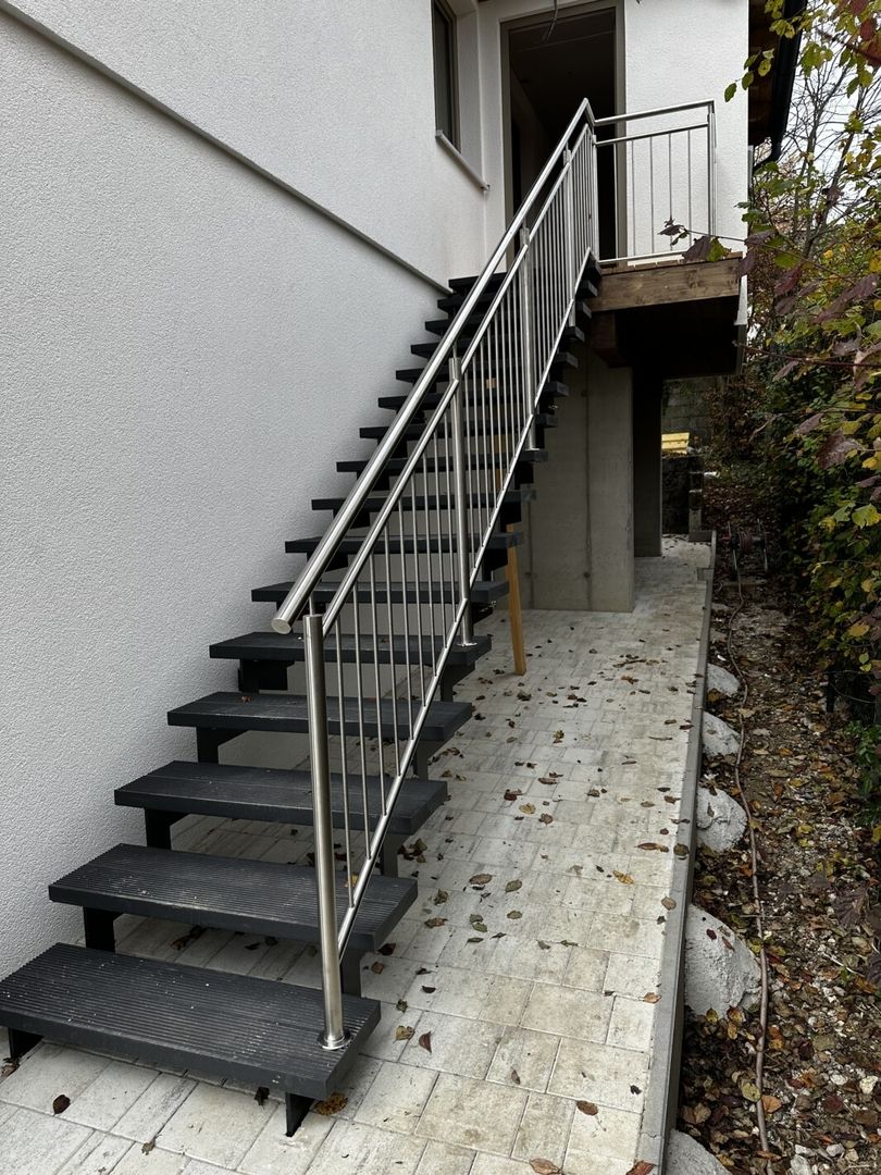 Eine schwarze Stahlwangentreppe mit Stahlgeländer an einer weißen Hauswand