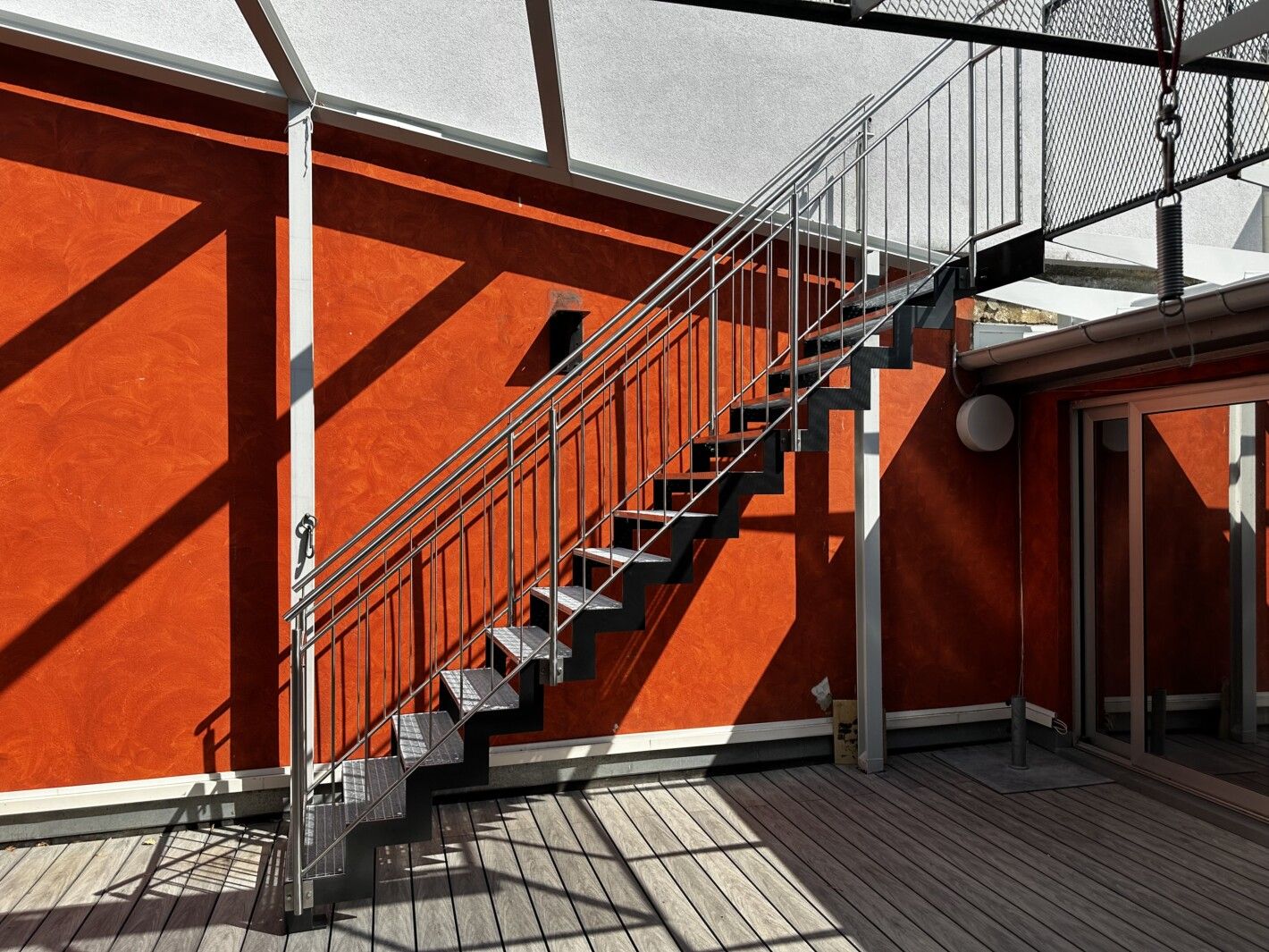 Eine Stahlwangentreppe mit Gitterrosttrittstufen an einer orangenen Hauswand