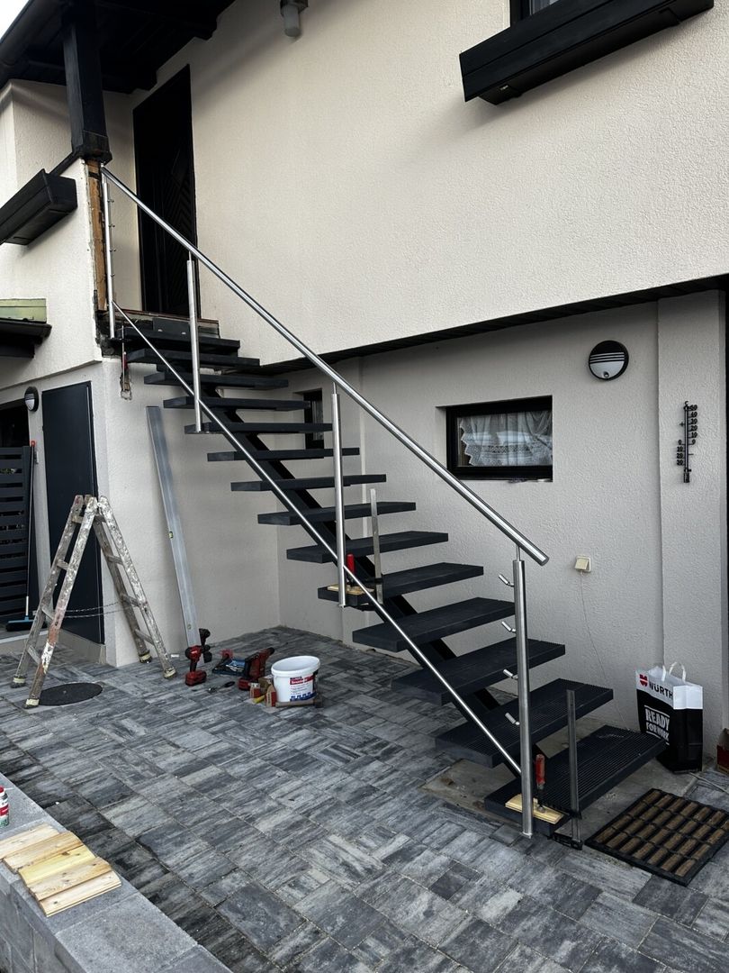 Eine schwarze Mittelholmtreppe mit Metall Geländer führt zu einer Haustüre