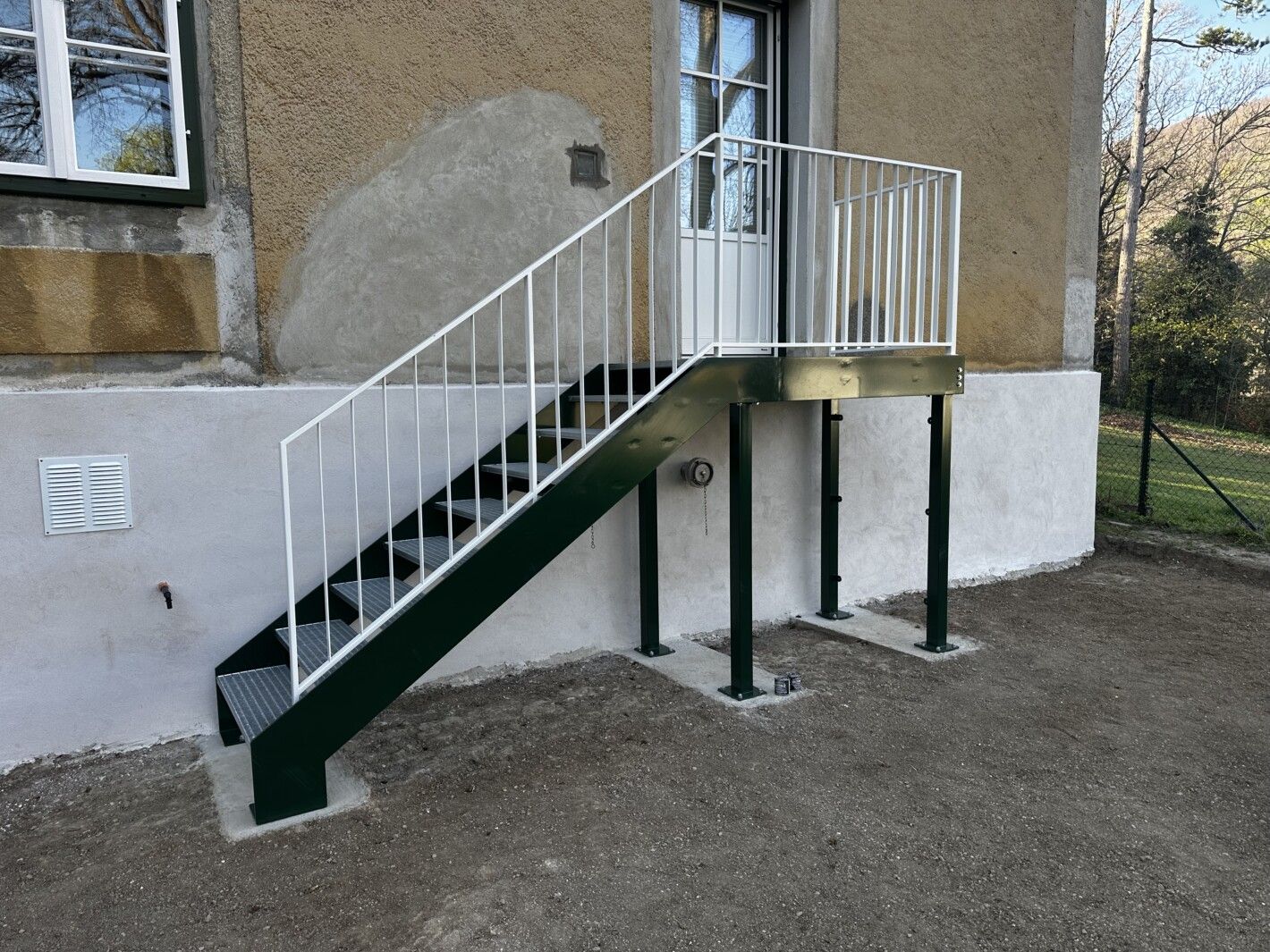 Eine Stahlwangentreppe mit Podest und einem weißen Geländer vor einem Hauseingang