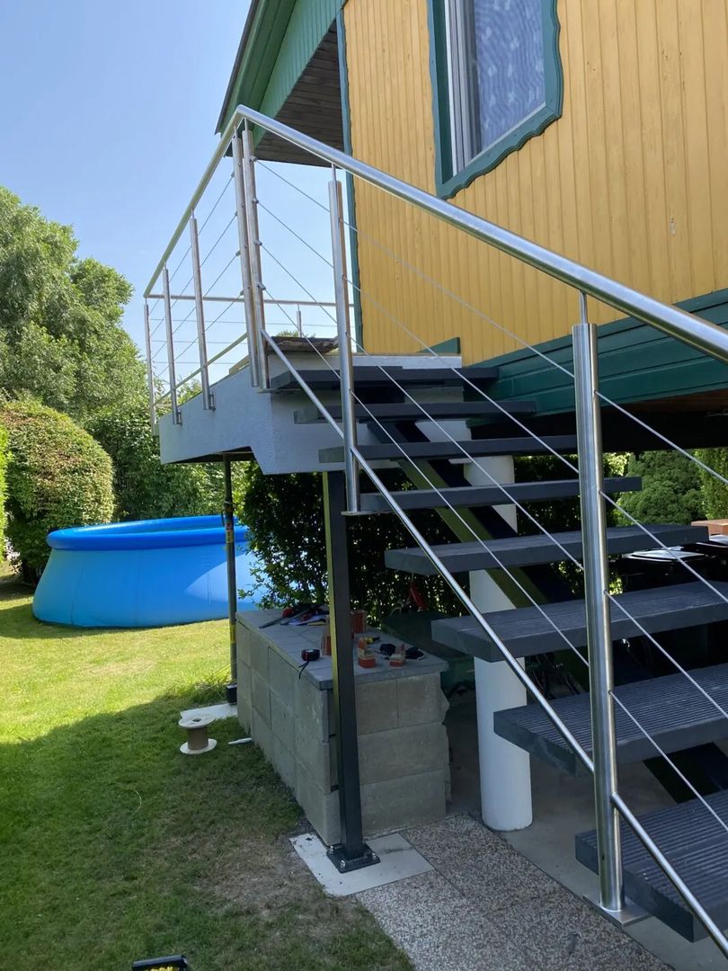 Mittelholmtreppen aus Metall mit silbernem Geländer an einer Hauswand